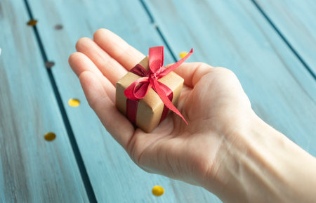 Hands holding little gift with red bow. Close up.の写真素材