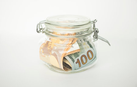 Many 100 US dollars bank notes in a glass jar isolated on white backgroundの写真素材