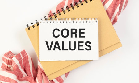 Notebook with text inside Core Values on table with coffee, laptop and some sheet of papers with chartsの写真素材
