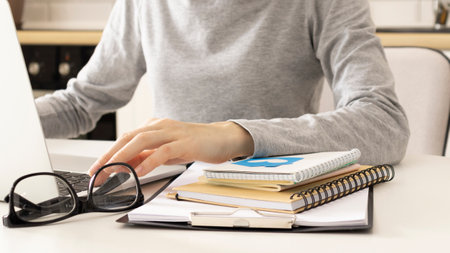 Hands of a female freelancer, working behind the table at home. She's typing something on a laptop keyboard.の写真素材