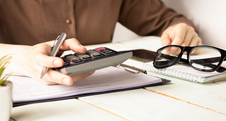 Close up of woman's hands writing in spiral notepad placed on wooden desktop with various items