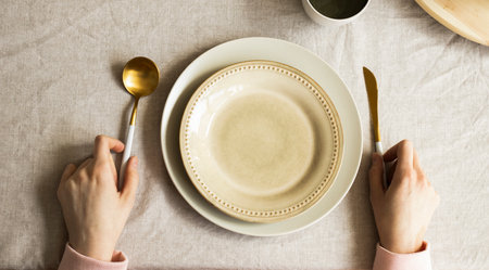 Female hands hold fork and knife on wooden background with plate, top view