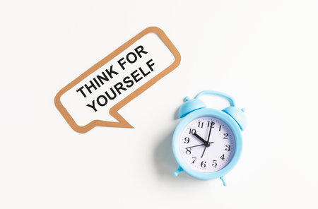 THINK FOR YOURSELF is written on the chalkboard next to the white alarm clock, glasses, potted plant, and pencils in a stand.の写真素材