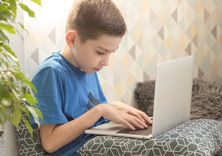 Picture of preteen boy using a laptop for playing online games and wearing headphone at home