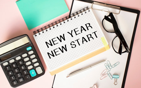 Notepad with NEW YEAR NEW START text on the office table with glasses, calculator, notepad and paper clips.の写真素材