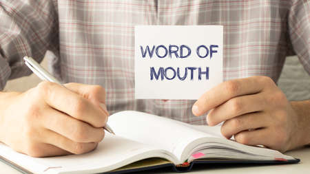 man take a paper with text Word Of Mouth on the shirt with office backgroundの写真素材