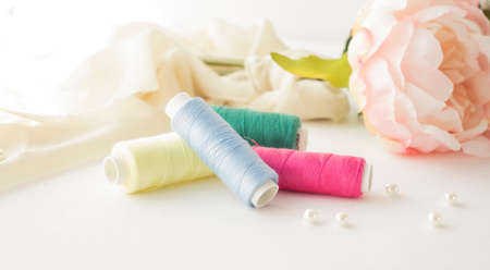 Threads on spools of different colors lie on a light wooden table. Three spools of thread are lying.