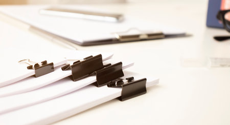 Hands of businessman hold pen for work in stacks of paper files, information search for business reports and heaps of incomplete documents is achieved on a laptop computer table in a modern officeの写真素材