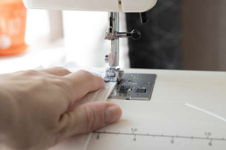 Woman hands using the sewing machine to sew the face medical mask during the coronavirus pandemia. Home made diy protective mask against virus.の写真素材