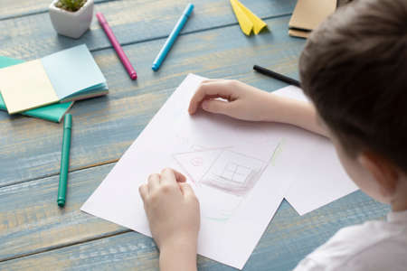 A child hand with pencil is drawing picture of country house