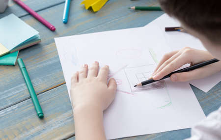 A child hand with pencil is drawing picture of country houseの写真素材