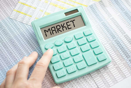 The word MARKET is written on the calculator. Business man holding a calculator in his hand. Top view of the desktop and business charts. Finance or business concept.の写真素材