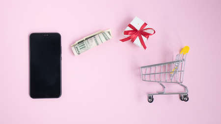 Flat lay of mobile phone red gift box and shopping cart on pink background with copy space. Christmas holiday and online shoppingの写真素材