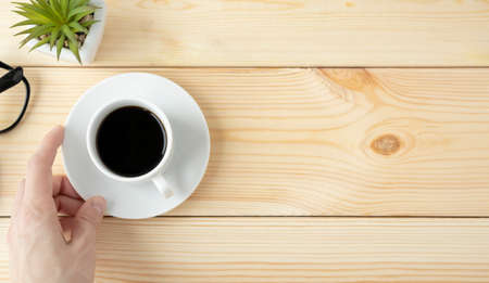 Woman holding a cup of hot coffee on a wooden table, hand with a mug and a flower, top view. Banner, place for textの写真素材