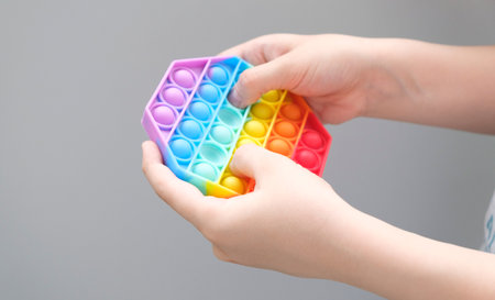 Anonymous child with colorful pop it game. Close up bunner shot of kid hands playing with colorful pop It fidget toy.の写真素材