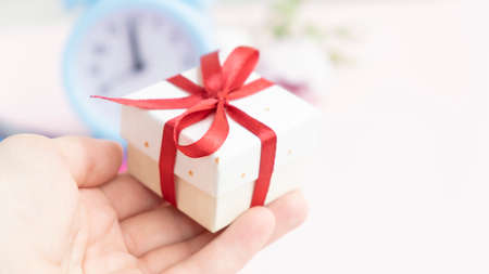 A girl in a white sweater holds a gift wrapped in craft paper with a red bow on a white background. Close-up, space for text.の写真素材