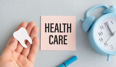 health care text on pink sticker with alarm clock and tooth figurine in palm