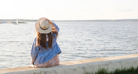 girl in hat and blue dress sitting on a sandy beach, picnic.の写真素材