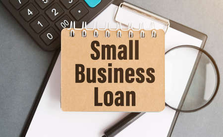SMALL BUSINESS LOAN. blank notebook with markers pen beside. The notebook is on paper with text....