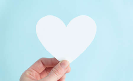 hand holding a white heart in blue background. Charity, pure love, compassion and kindness concept....