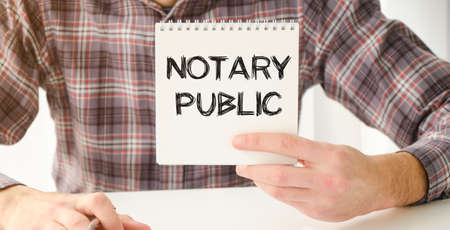 a woman in a white shirt holds a piece of paper with the text: notary public. business concept for companiesの写真素材