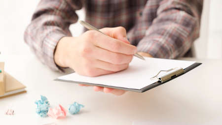 Close up young businessman standing near table with pen in hands, ready signing profitable offer agreement after checking contract terms of conditions, executive manager involved in legal paperwork.の写真素材