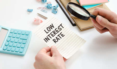 Magnifying glass on colourful pie chart with Low Interest rates text on paper, dice, spectacles, pen, laptop calculator on wooden table - business, banking, finance and investment conceptの写真素材