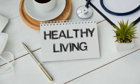 HEALTHY LIVING text in a notebook. A medical protective mask and a thermometer are on the notebook.の写真素材