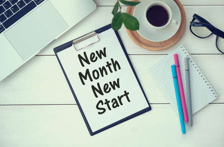 Office workplace with coffee cup, calculator, stationery and plant. Text NEW MONTH NEW START on white notepad page. Table desk top view, flat layの写真素材