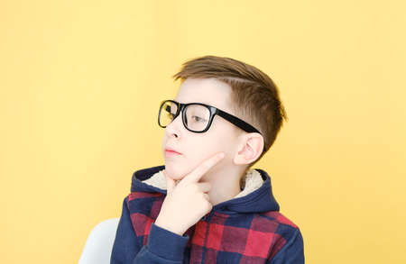 pensive boy with blonde hair and glasses isolated on yellow.の写真素材