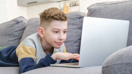 Young kid with a laptop on the couch, relaxing on couch with gadgets.の写真素材