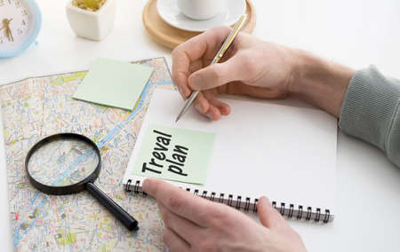 Hand writing travel plan in a lined spiral notepad arranged on a map.