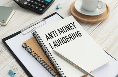 Anti-money laundering AML text on a clipboard on light background with charts paper.