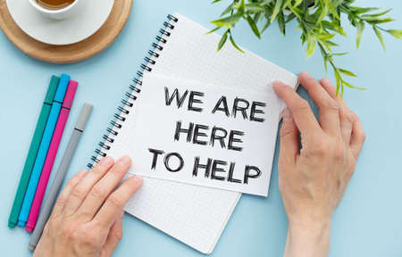 we are here to help. text on open notepad on blue background near white kup coffee.の写真素材