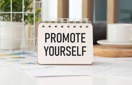 A sign with the inscription PROMOTE YOURSELF on the table with office supplies.の写真素材