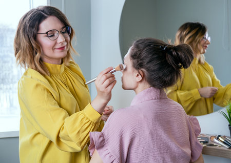 Beauty stylist applying make-up to a young model.Professional Make-up artist doing glamourの写真素材