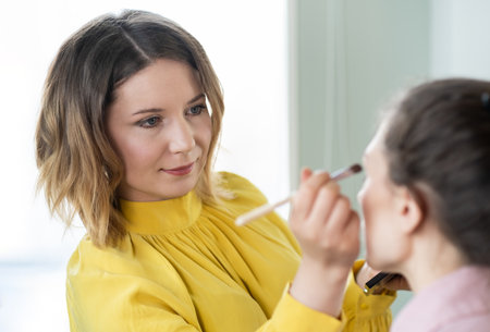Beauty stylist applying make-up to a young model.Professional Make-up artist doing glamour