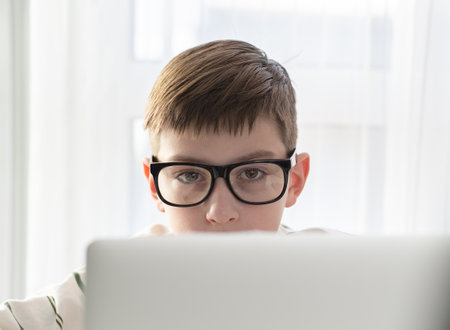 Portrait of a boy in glasses hiding behind a laptop. The concept of online learning, online consultations.の写真素材