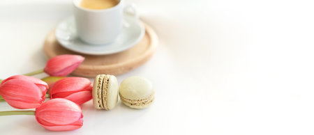 Close up of sweet french macarons, cup of tea or coffee and spring flowers on white background. Space for textの写真素材