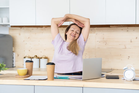 Woman attractive blonde in the workplace stretches sitting at the desk in the office.