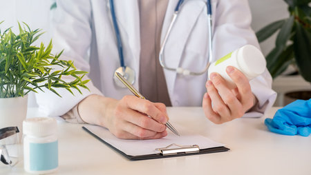 Female black medicine doctor hand hold jar of pills and write prescription to patient at worktable. Panacea and life save, prescribing treatment legal drug store concept. Empty form ready to be usedの写真素材