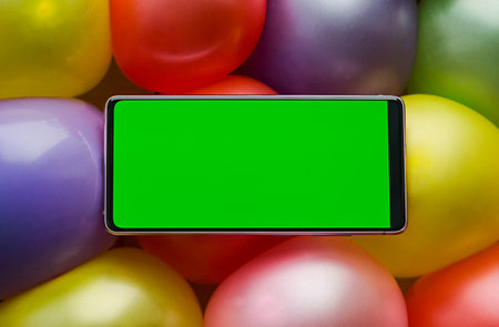 Mobile phone with a green screen lying on colorful balloonsの写真素材