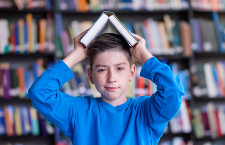 Invest in knowlenge Concept, schoolboy boy looks at the camera with a book over his head against the backdrop of the library hallの写真素材