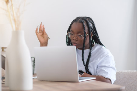 Portrait of young smiling black woman in wireless headset holding using digital tablet sitting on chair in living room.の写真素材