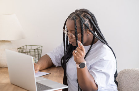 Portrait of young smiling black woman in wireless headset holding using digital tablet sitting on chair in living room.の写真素材