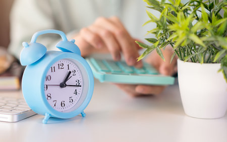 Blue Alarm clock and calculator on table with blur woman hand calculating in foreground, tax time...