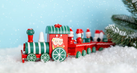 A red and green train stands on the snow on a blue snowy background. Christmas and New Year...