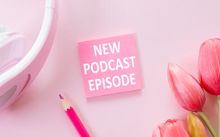 NEW PODCAST EPISODE text on notepad next to headphones, podcasting concept on pink backgroundの写真素材