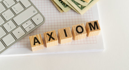 Wooden blocks spell AXIOM on a notebook, surrounded by a keyboard and money. Neatly arranged and well-lit, suitable as a stock photo for business concepts and financial success.の写真素材