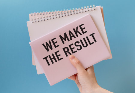 Close-up of pink notebook with text WE MAKE THE RESULT in womans hand on blue background, symbolizing determination, hard work, and achieving goals in business and personal life.の写真素材